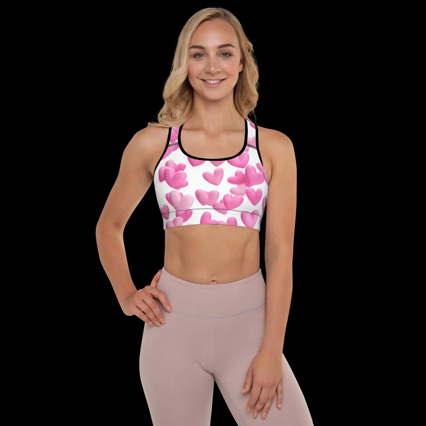 Woman wearing LOVE BATTLE Padded Sports Bra with pink heart design and racerback on black background